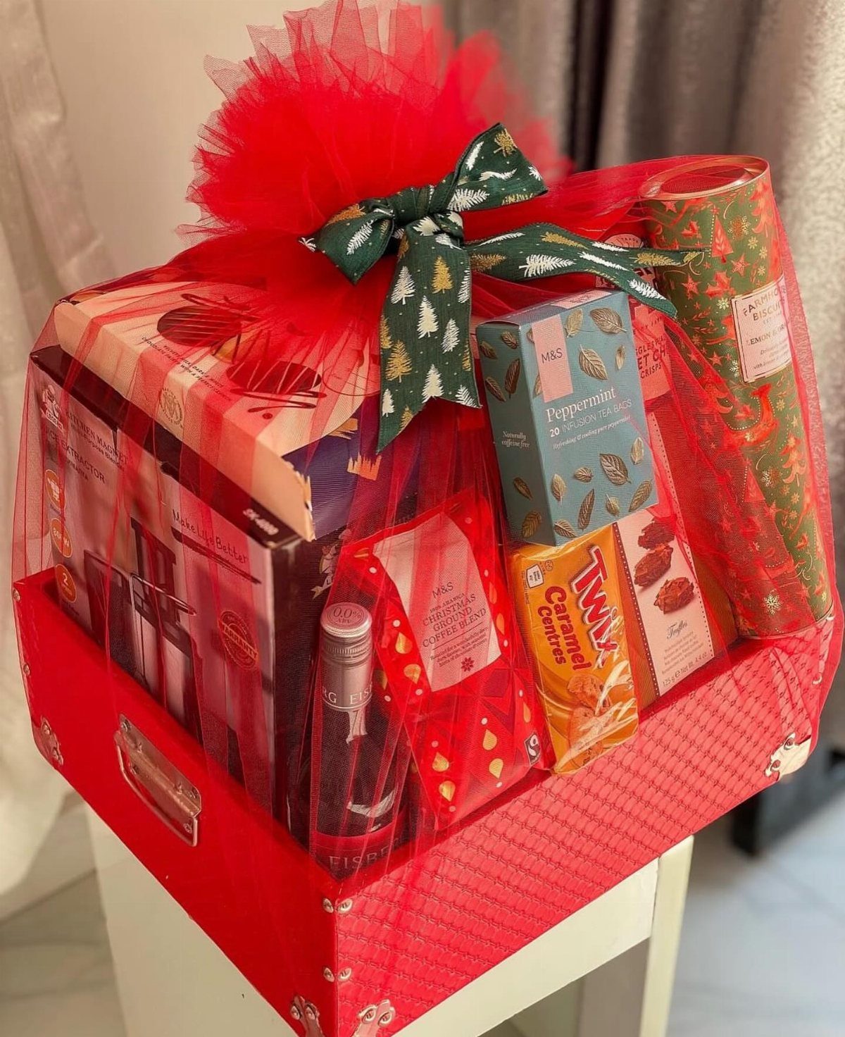 Red Christmas gift basket filled with sweets and wrapped in red tulle.