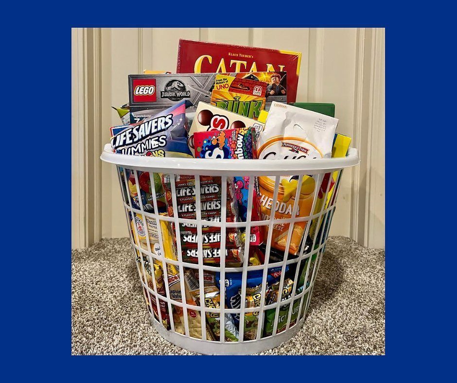 White laundry basket filled with Catan board game, LEGO, and assorted snacks.