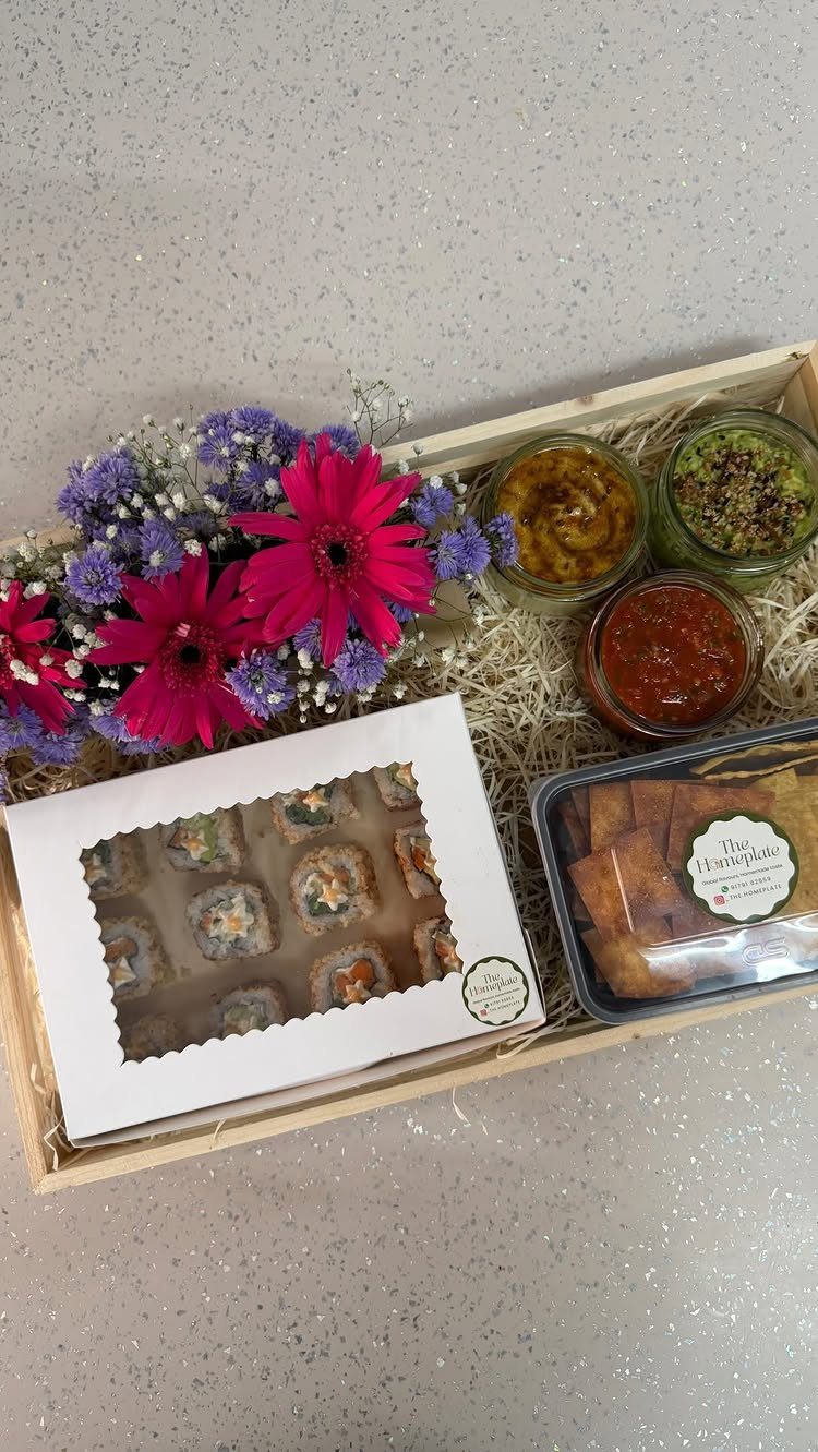 Wooden gift crate with gourmet condiments, pastries, treats, and colorful fresh flowers.