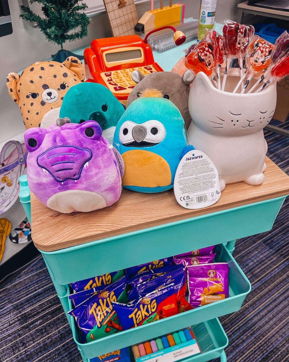 Turquoise rolling cart filled with plush toys, snacks, and school supplies.