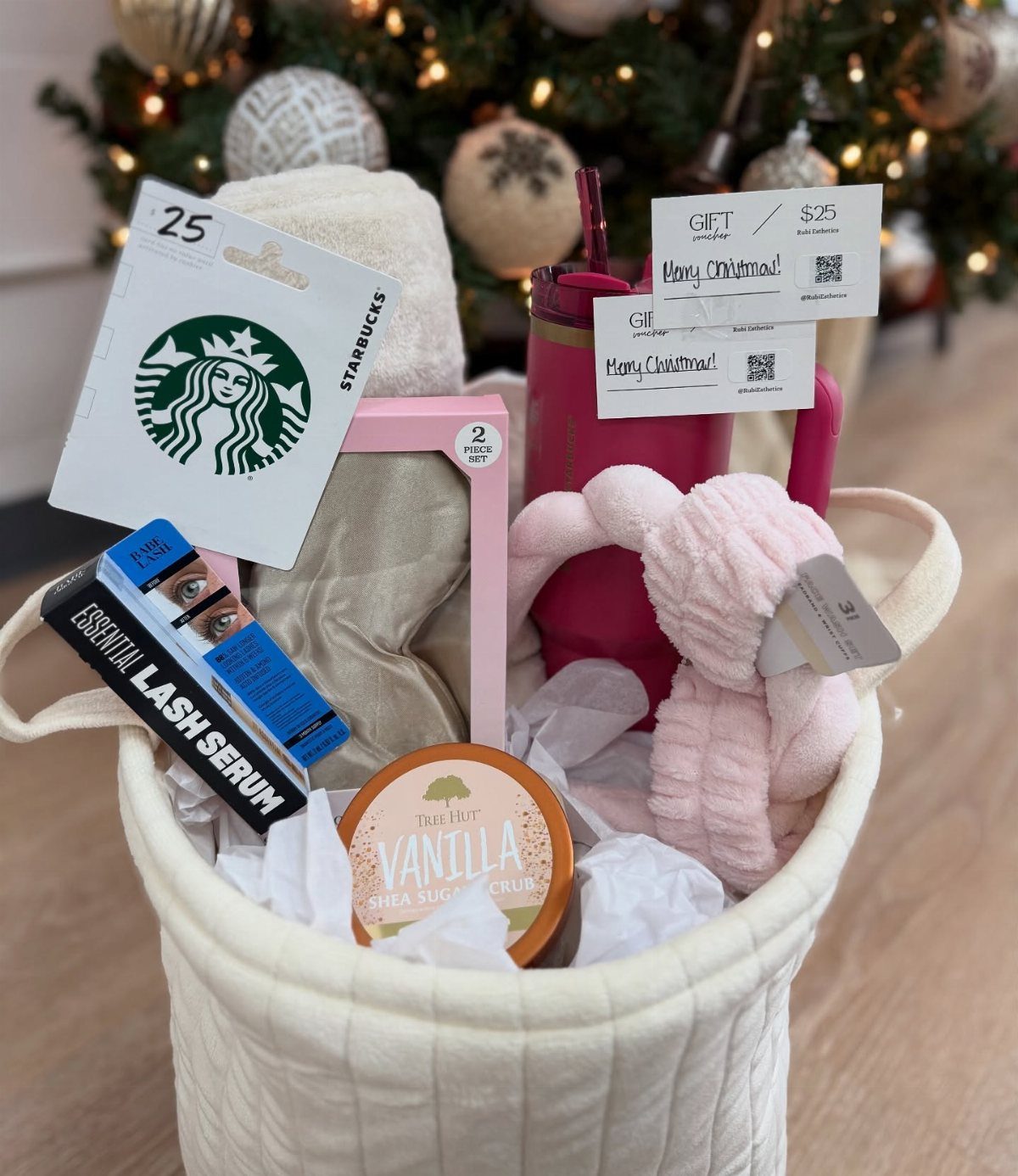 White gift basket containing spa products, a pink headband, and a Starbucks gift card.