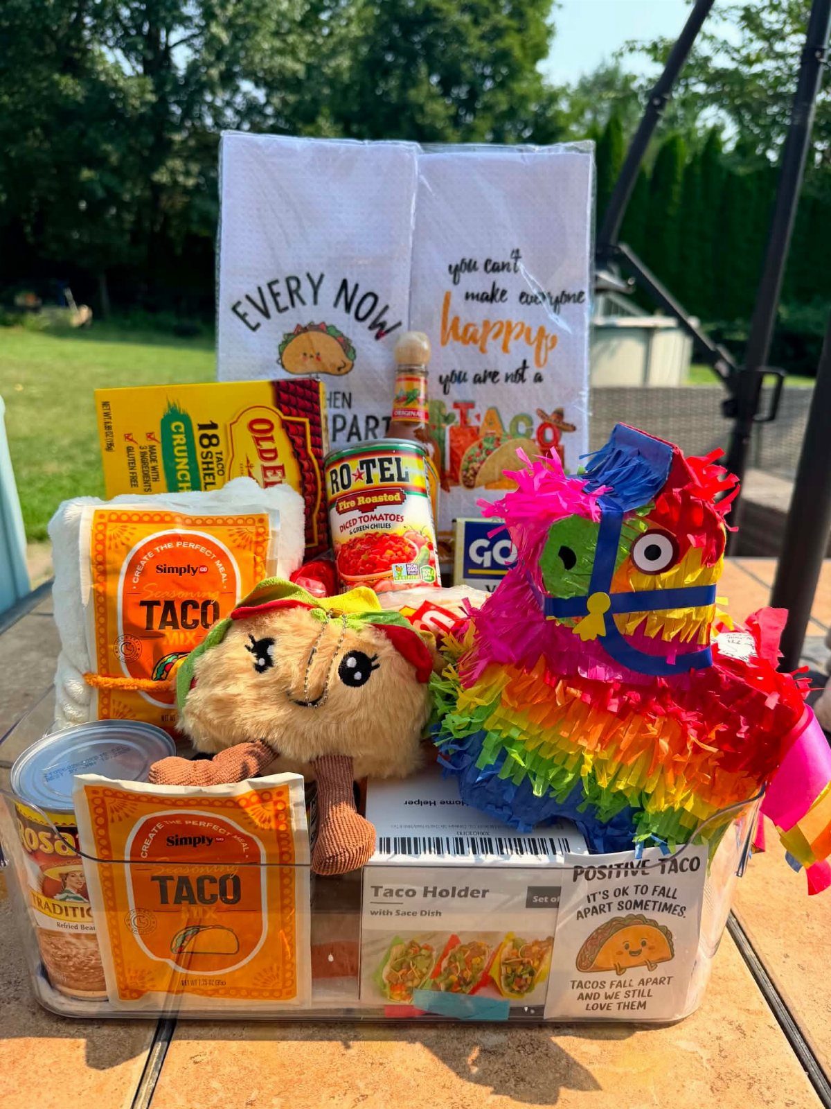 Taco-themed gift basket with shells, canned tomatoes, plush taco, and a colorful piñata.