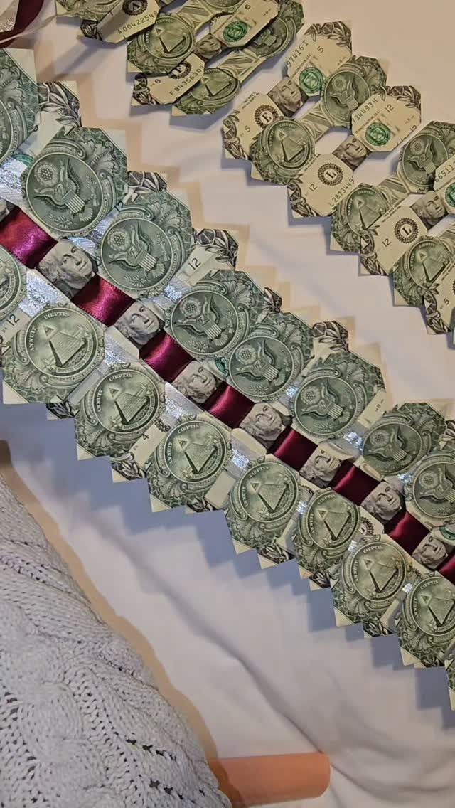 Dollar bill garlands with maroon ribbons laid on a white fabric background.