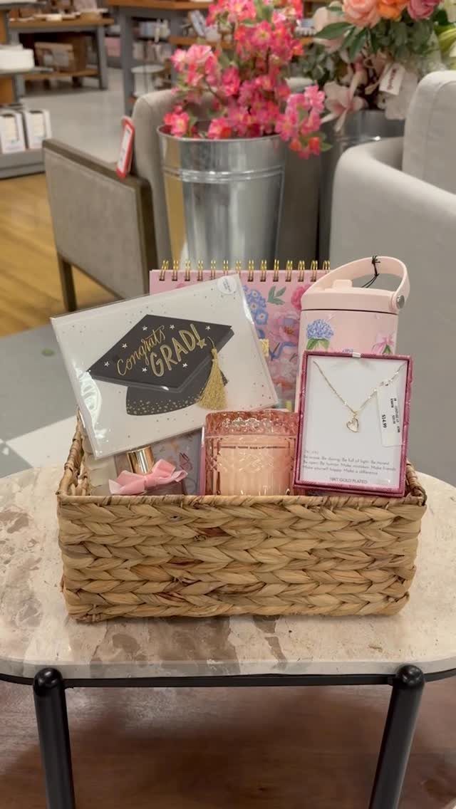 Woven gift basket with graduation card, pink notebook, and gold necklace on table