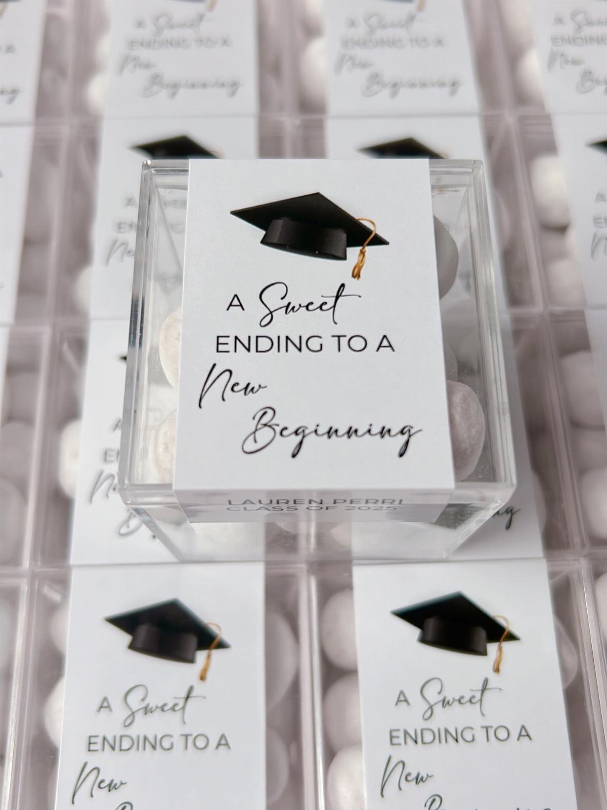 Clear plastic candy boxes with graduation themed labels and round sweets inside.