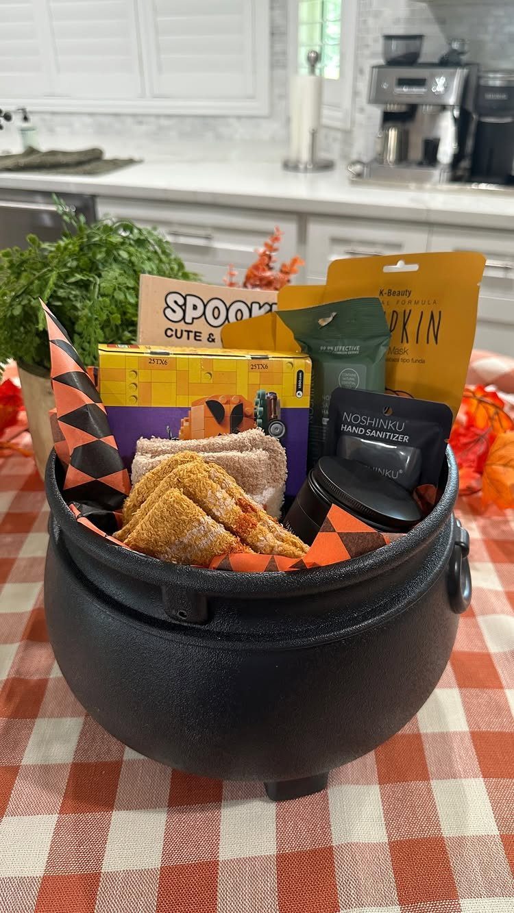 Black cauldron filled with Halloween treats on a red checkered tablecloth in a kitchen.