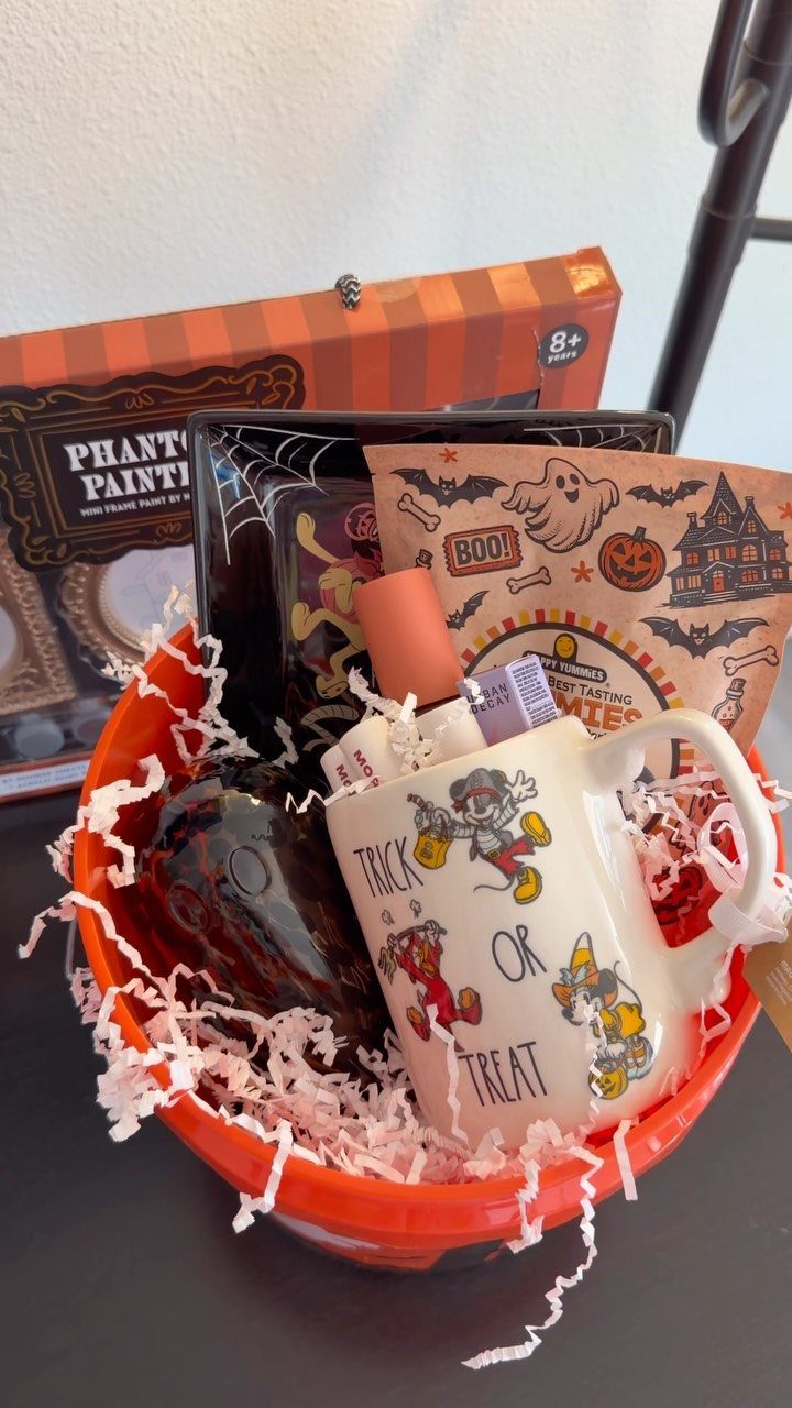 Orange Halloween bucket filled with a themed mug, snacks, and a painting kit.
