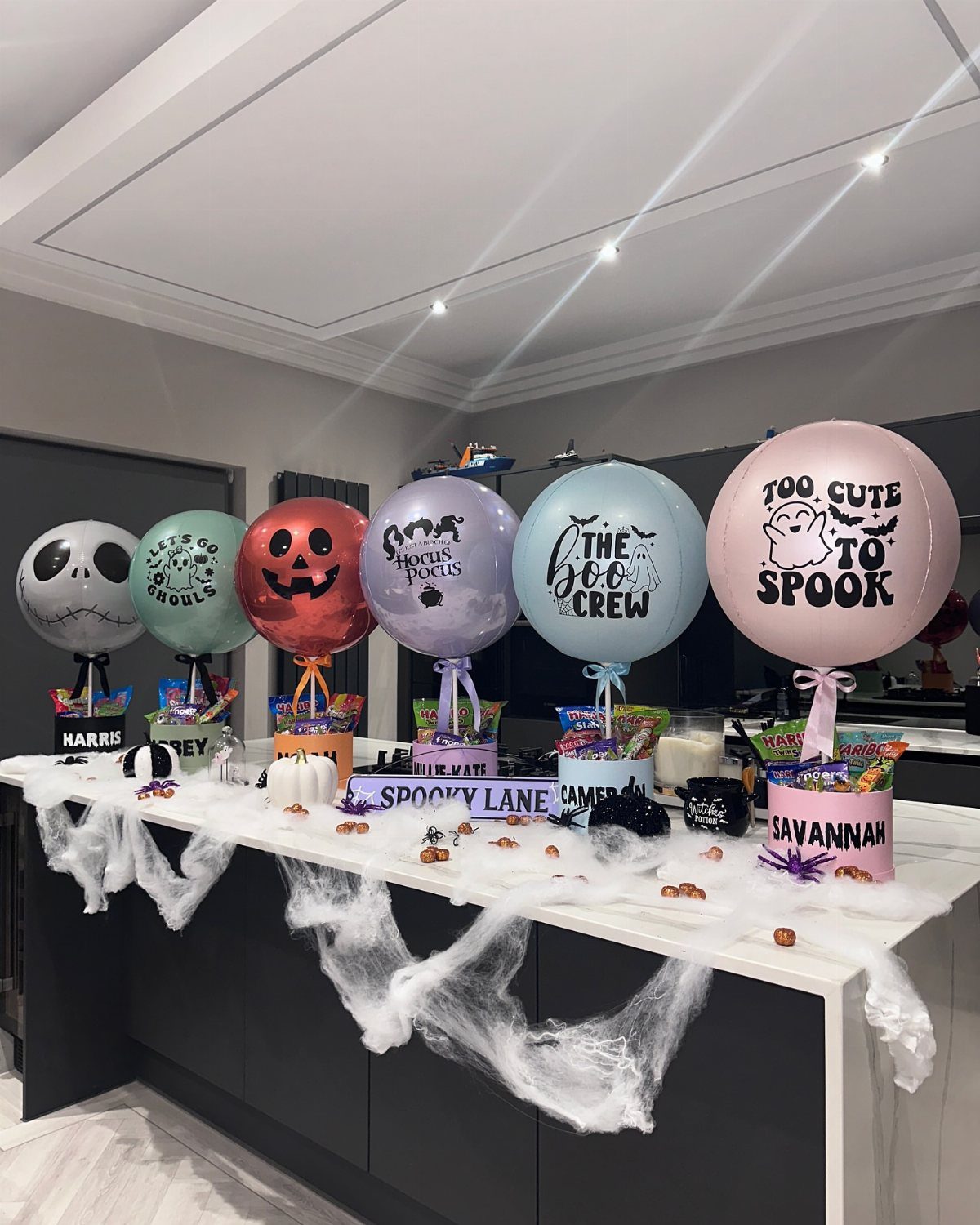Personalized Halloween boo baskets with colorful balloons on a white kitchen counter.