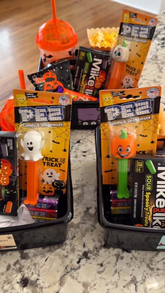 Two black Halloween boo baskets filled with candy, popcorn, and an orange drink.