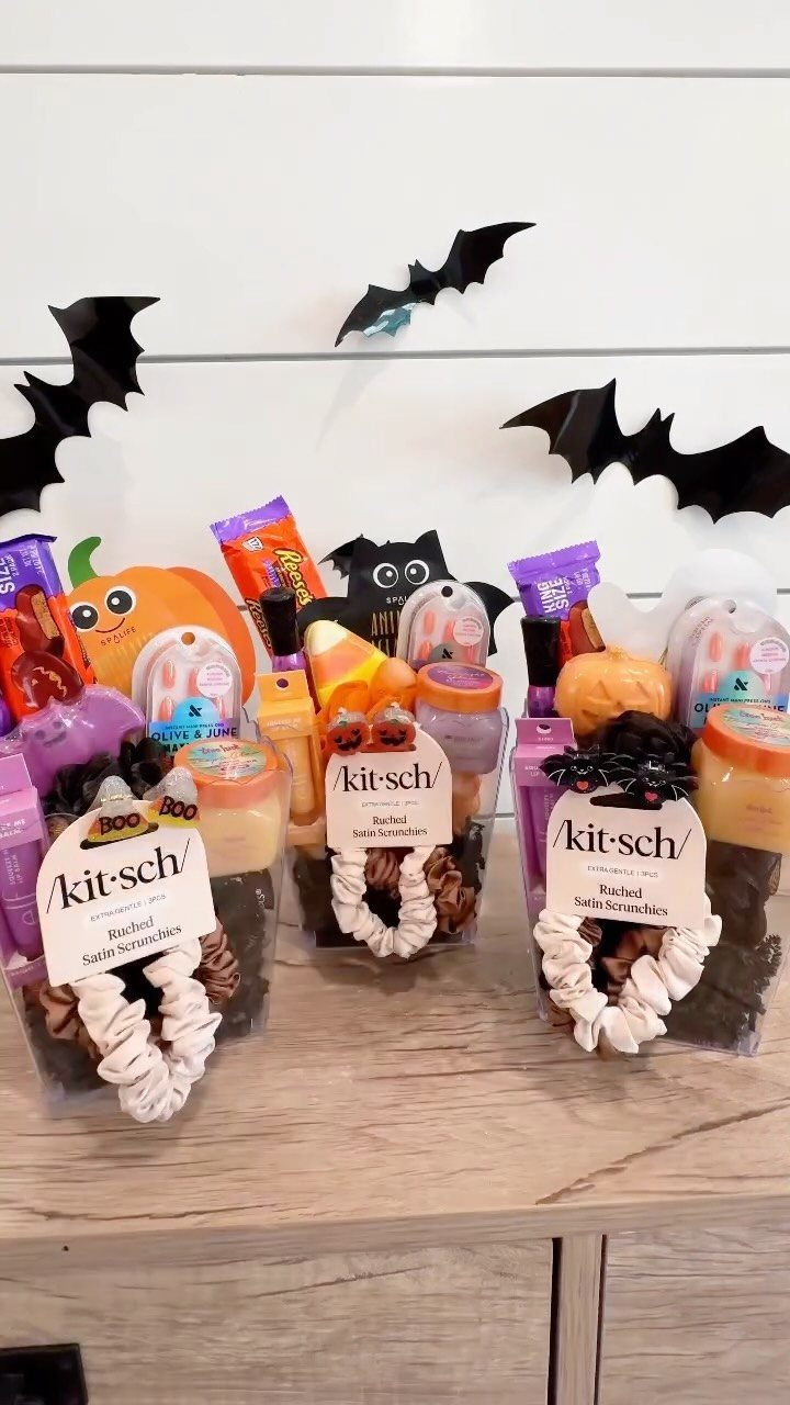Three Halloween boo baskets with scrunchies, skincare, and candy against a bat-decorated wall.