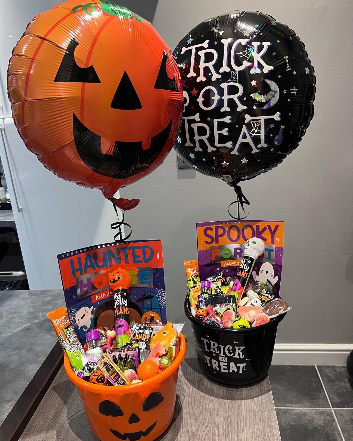 Two Halloween gift buckets filled with candy and topped with foil balloons.
