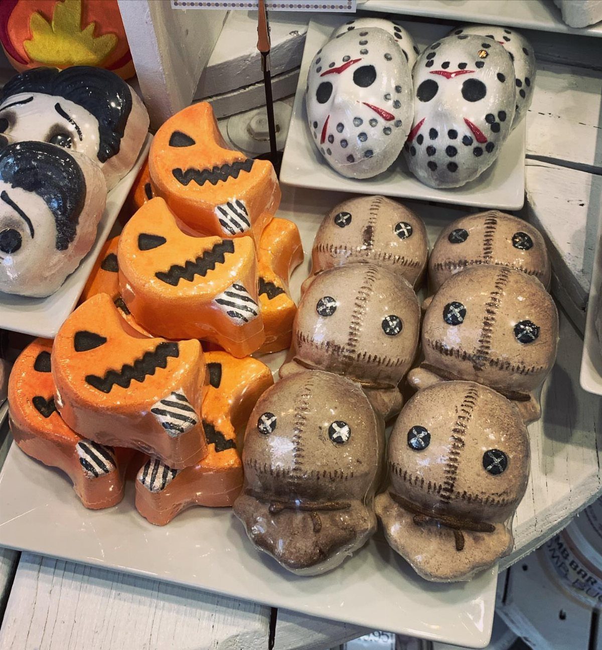 Halloween bath bombs shaped like pumpkins and horror characters on white plates.