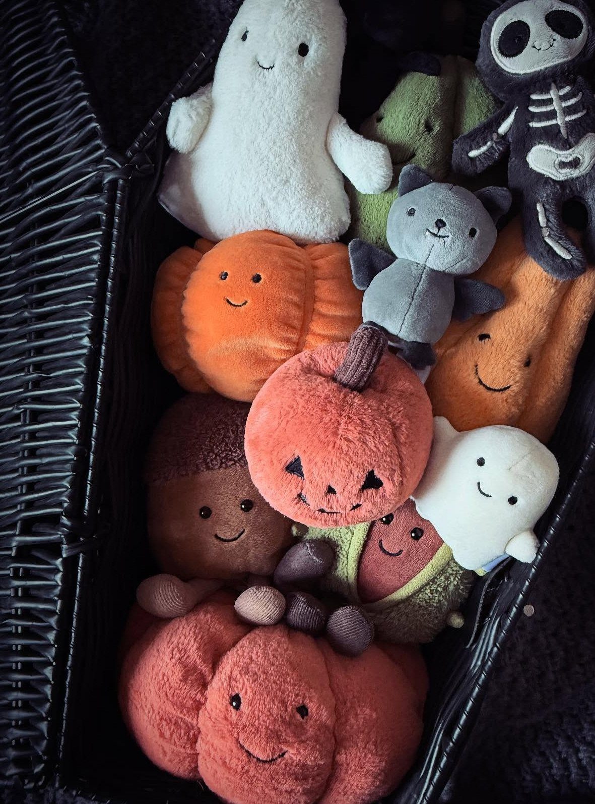 Halloween plushies including ghosts and pumpkins filling a black woven gift basket.