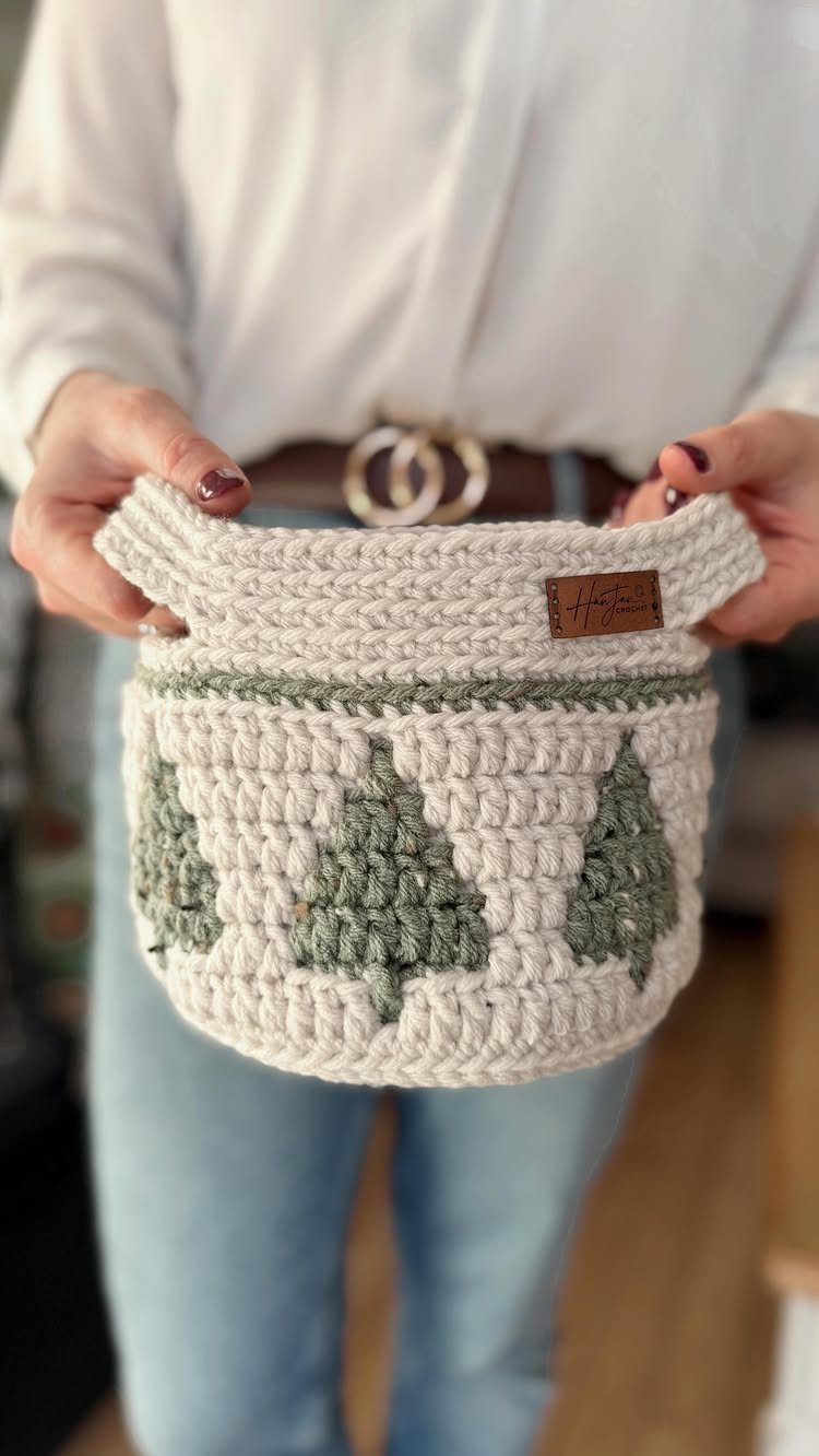 Handmade crocheted cream basket with green Christmas tree patterns held by a person.