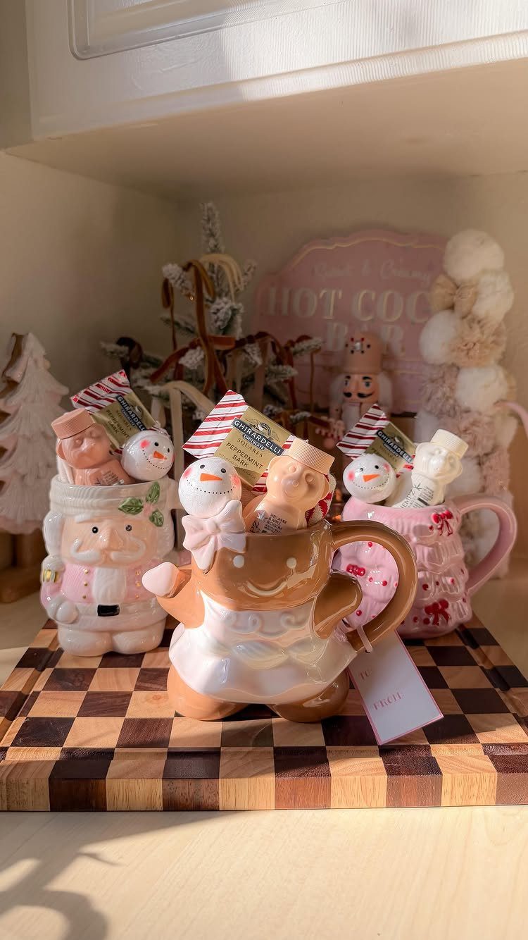 Festive ceramic holiday mugs filled with treats on a wooden checkerboard surface.