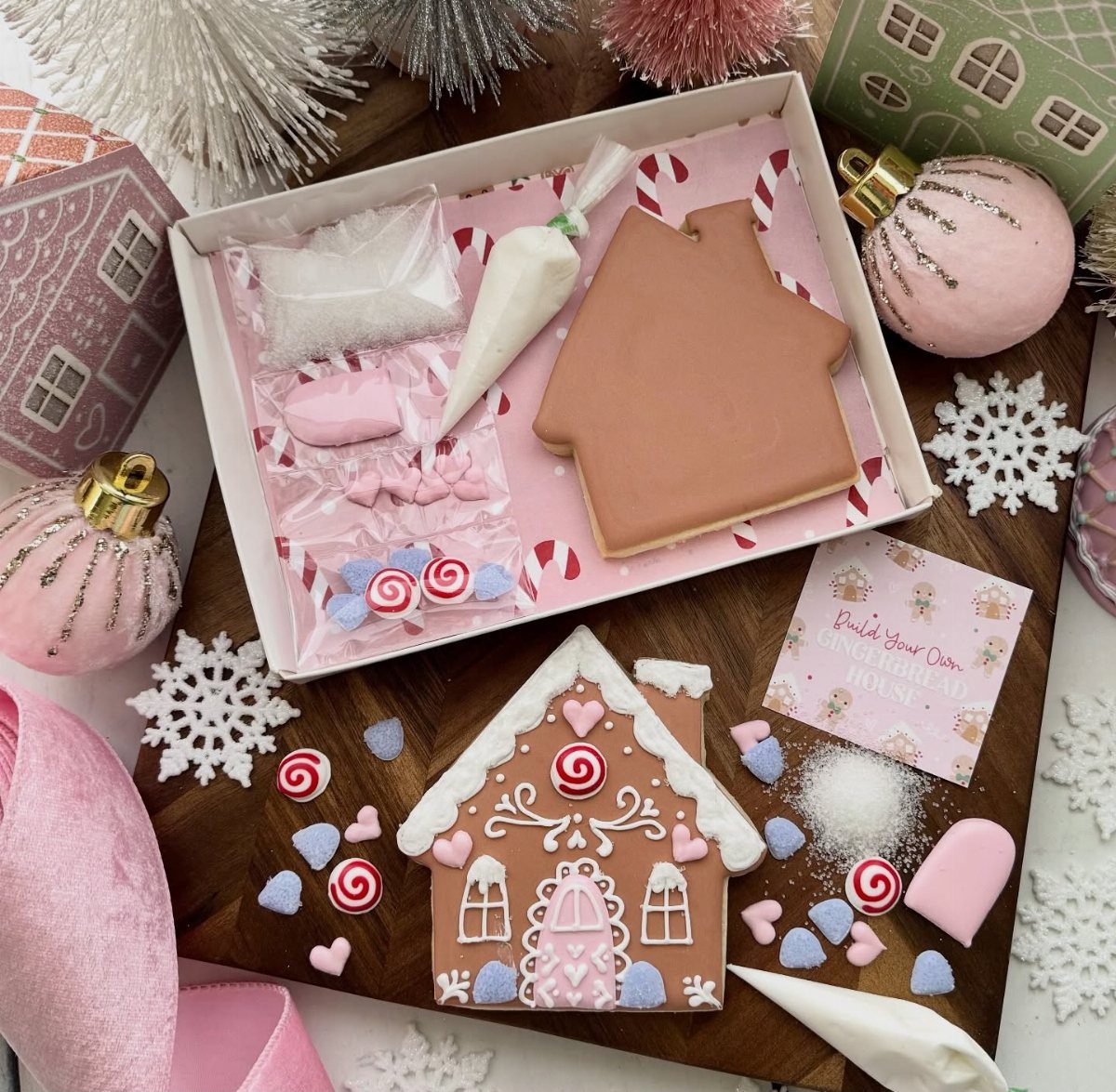 Gingerbread house kit with a decorated house, icing, and candies on wooden board.