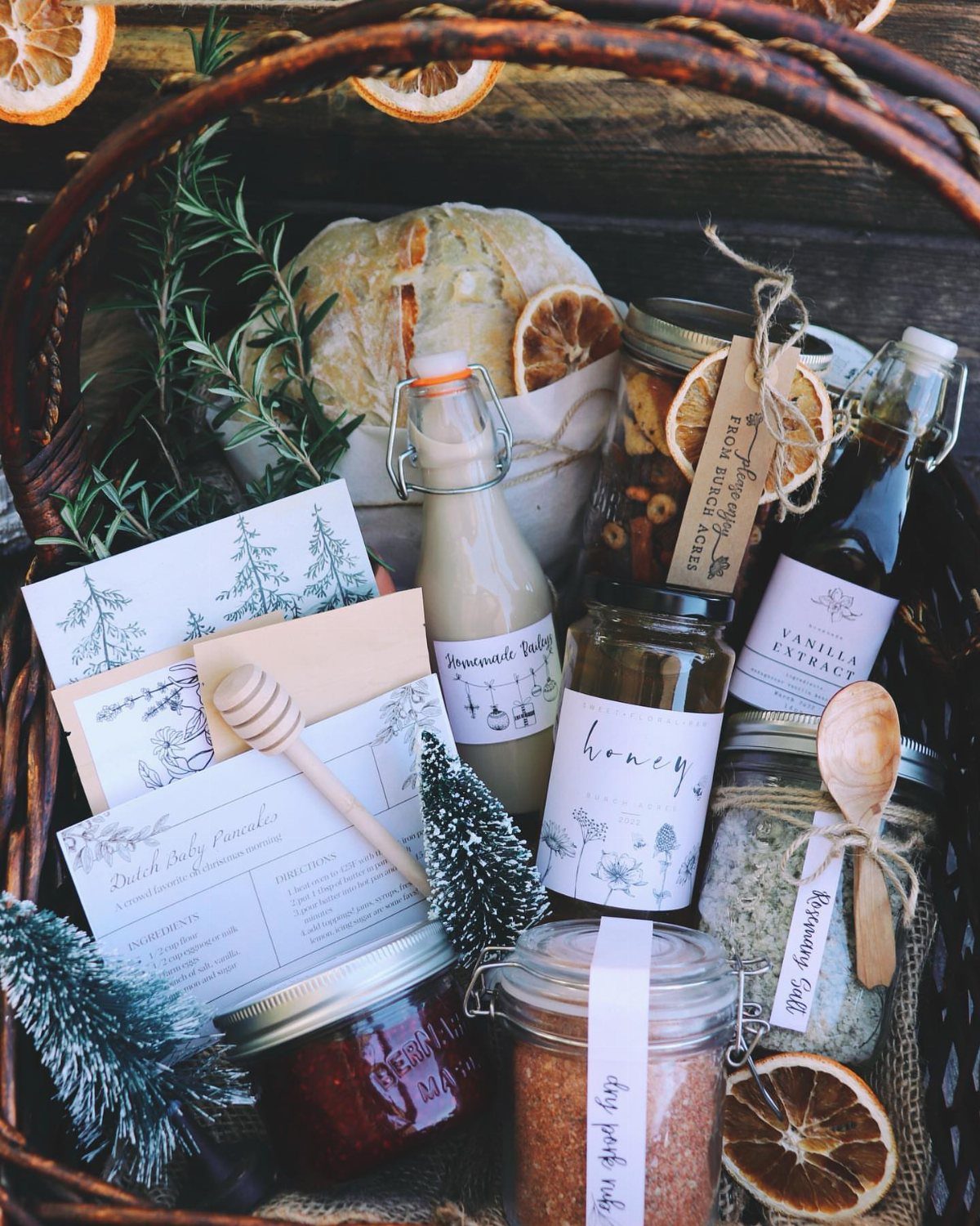 Wicker gift basket filled with gourmet jars, honey, vanilla extract, and dried oranges.