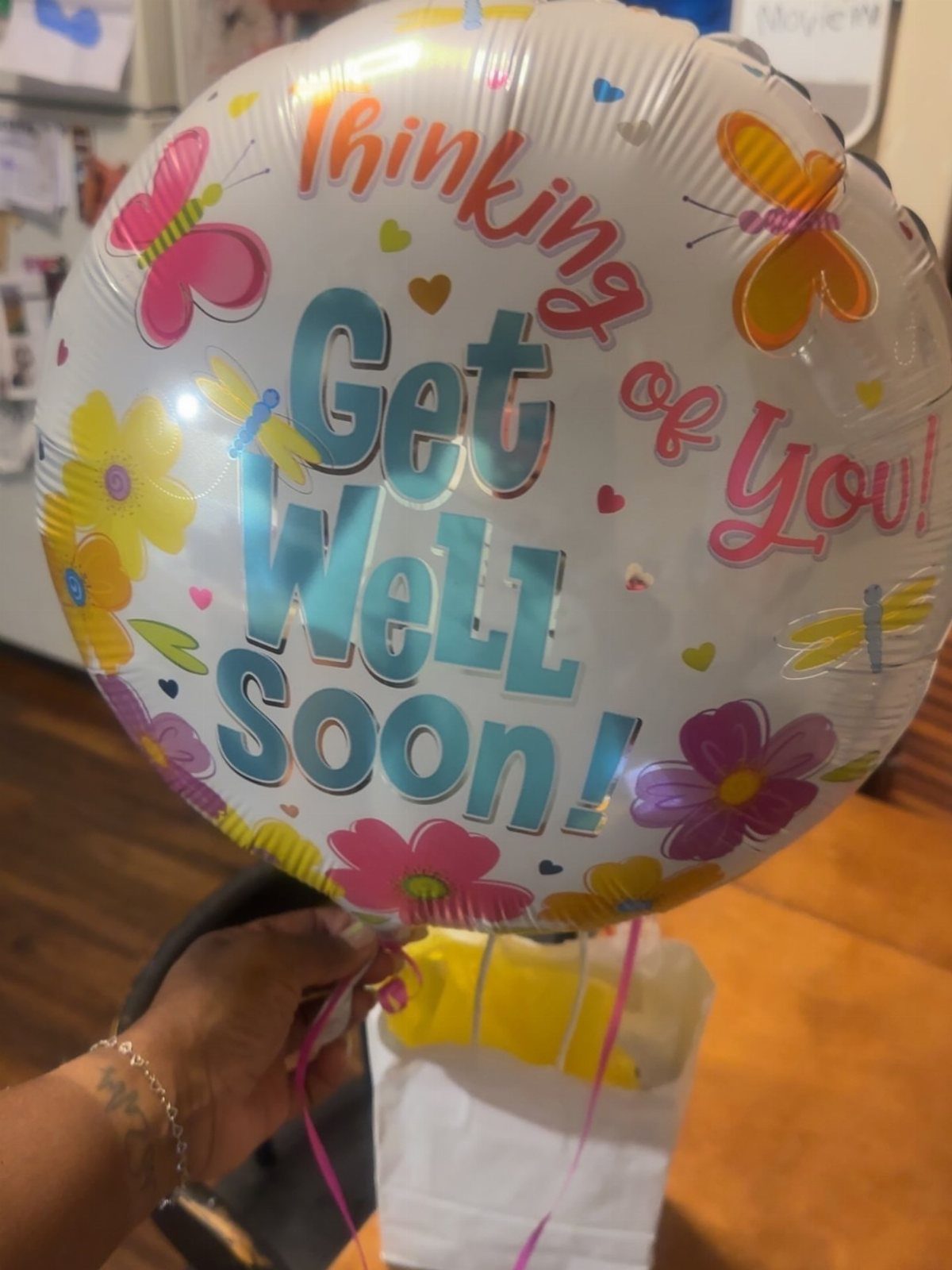 Get well soon foil balloon held above a white gift bag with yellow contents