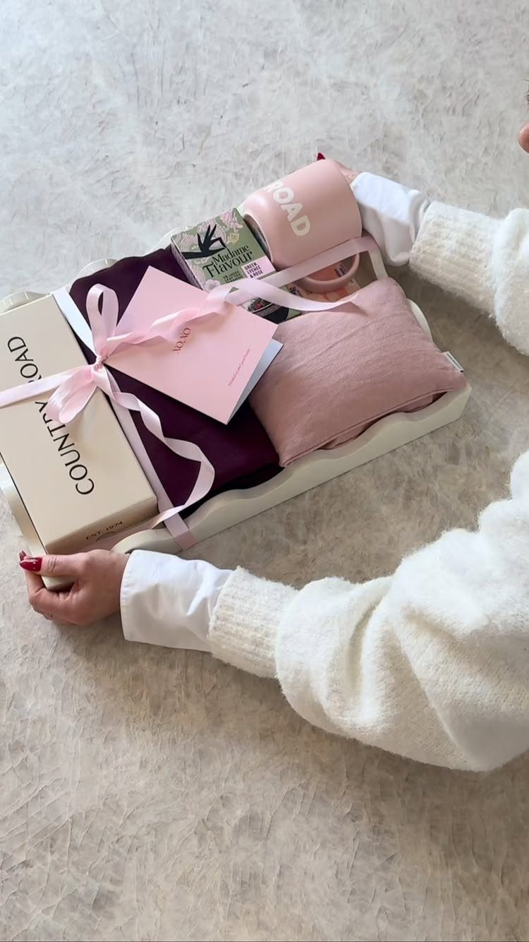 Gift tray with pink mug, blanket, and purple clothing held by a person.