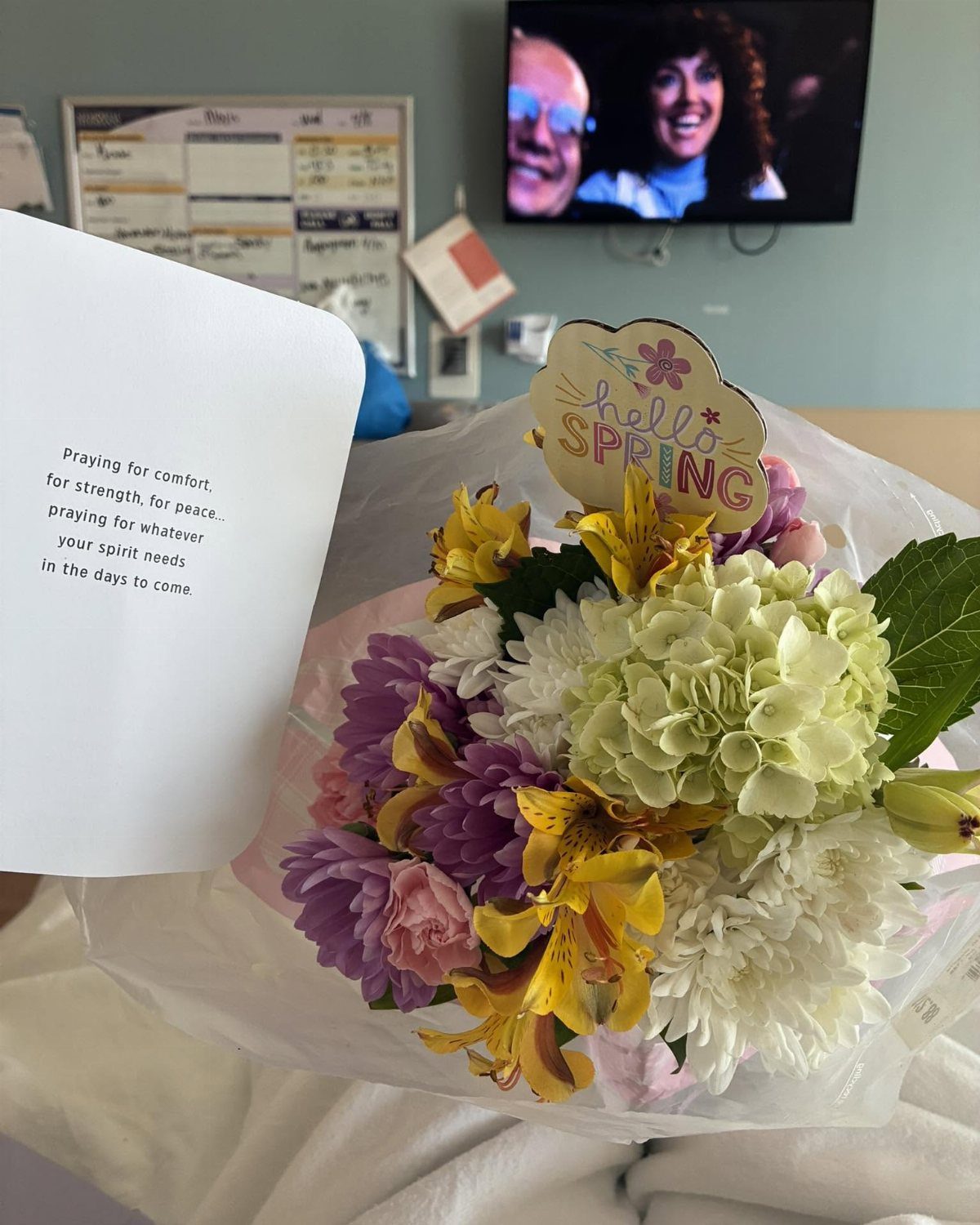 Colorful flower bouquet and a sympathy card on a white hospital bedsheet.