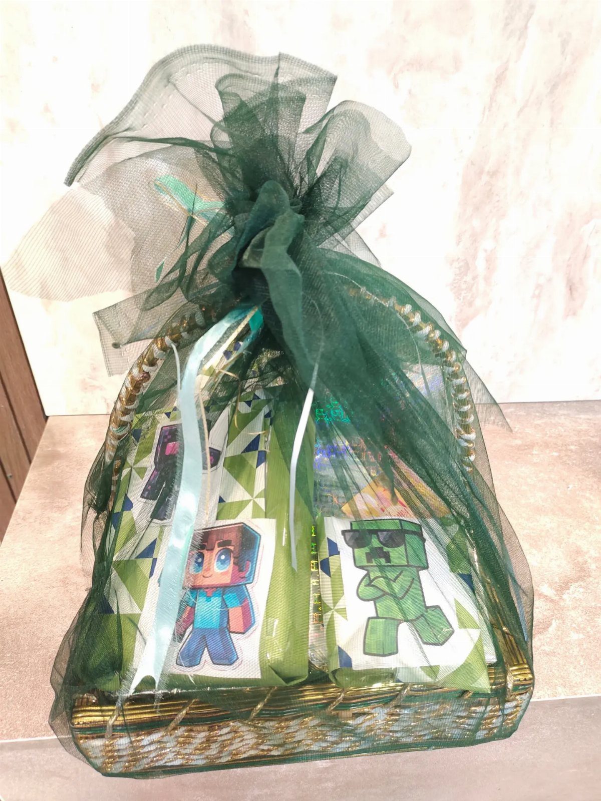 Wicker gift basket wrapped in sheer green tulle fabric tied with a bow.