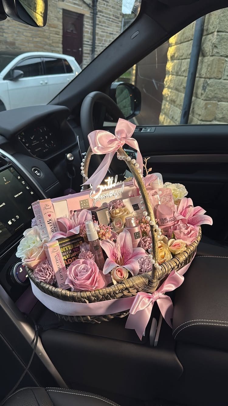 Wicker gift basket with pink flowers and cosmetics on a car seat
