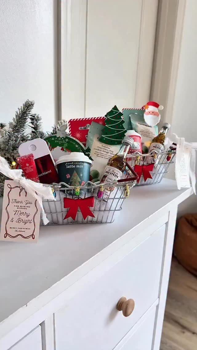 Two wire holiday gift baskets filled with treats and decorations on a white dresser.