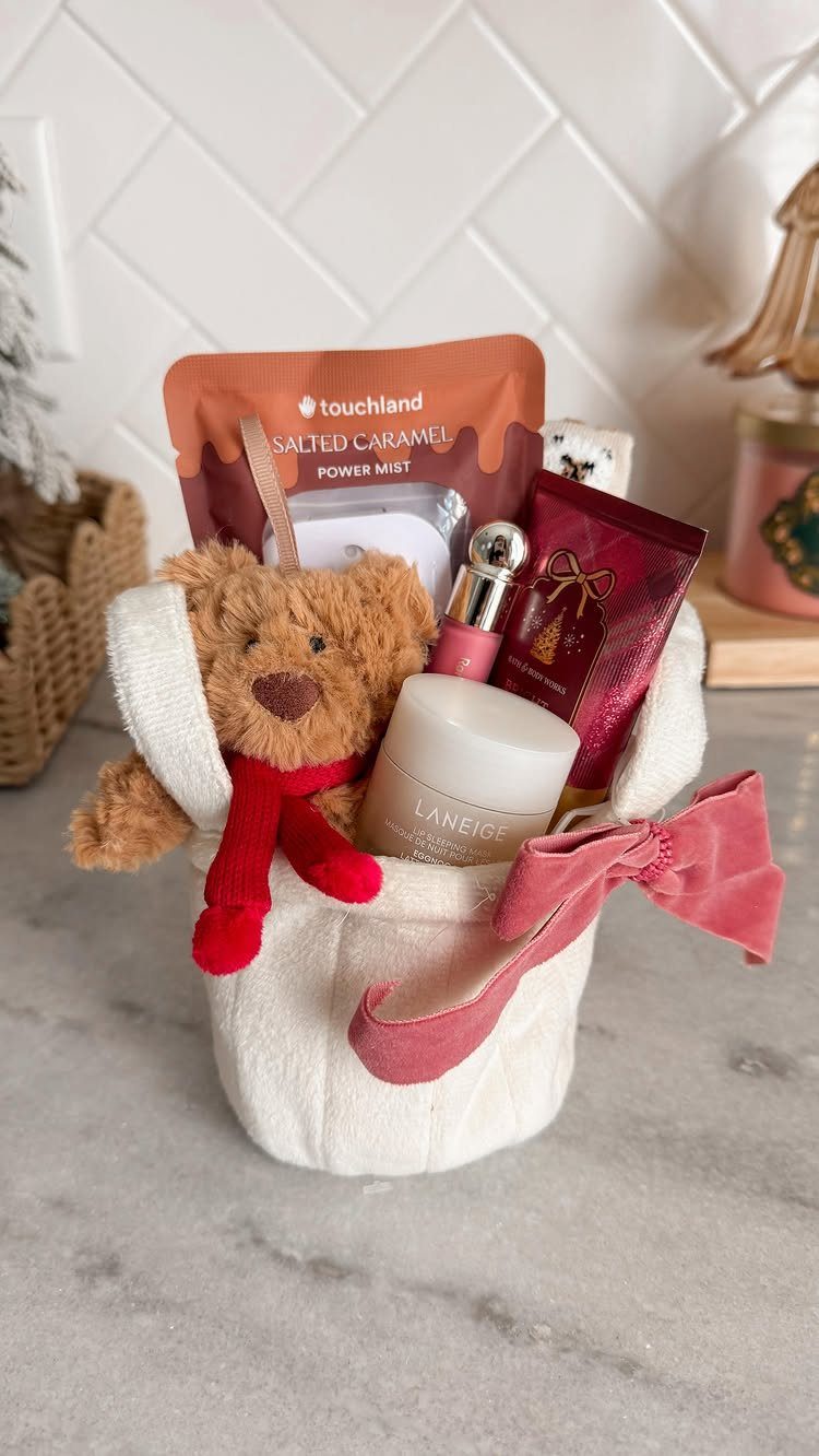 White fabric gift basket with a teddy bear, skincare products, and red bow.
