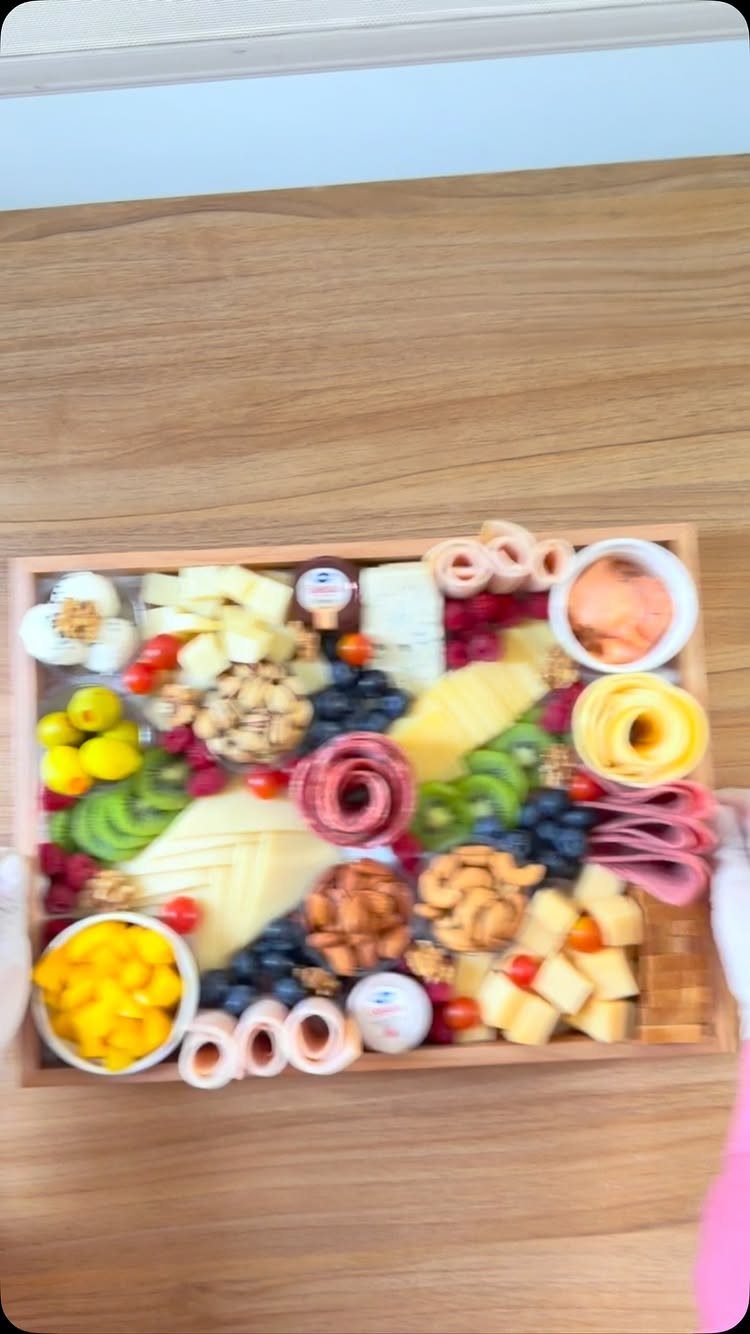 Charcuterie board with assorted cheeses, meats, fruits, and nuts in a wooden tray.