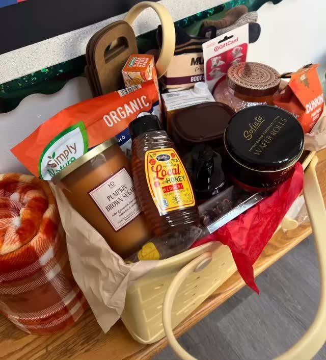 Gift basket containing honey, a candle, and snacks next to a plaid blanket.