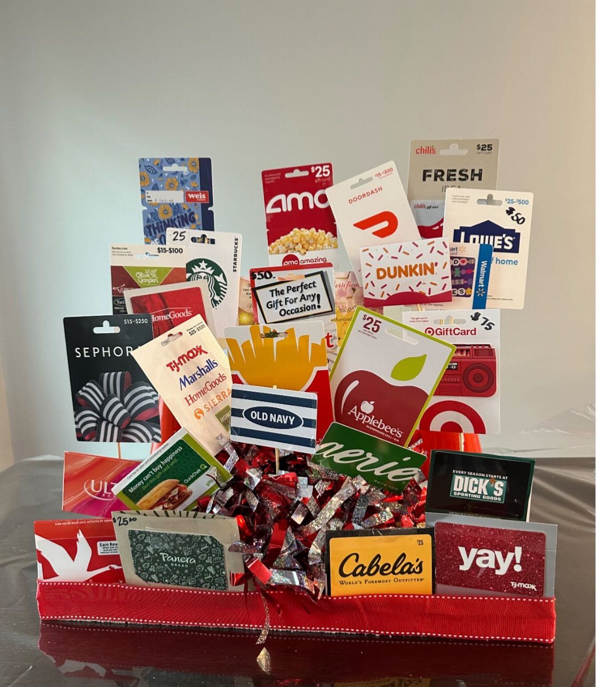 Various colorful gift cards arranged in a red basket with silver metallic filler.