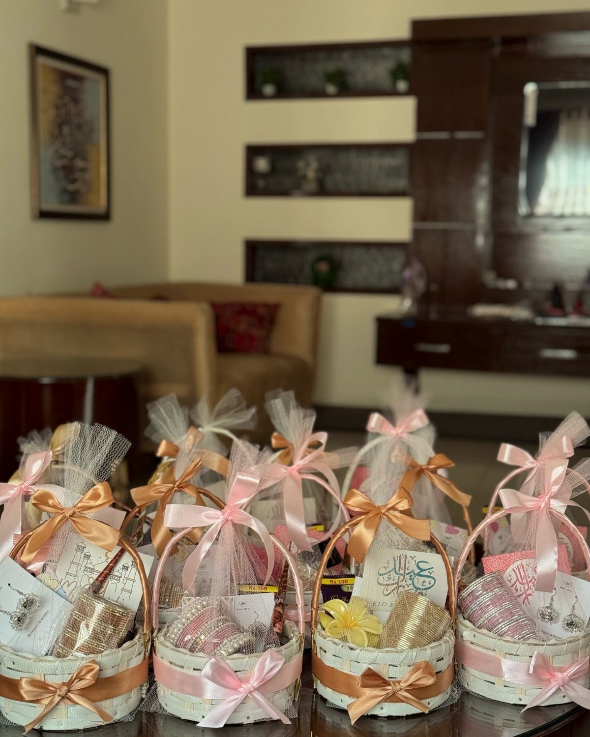 Small white gift baskets with pink ribbons and gold items wrapped in cellophane.