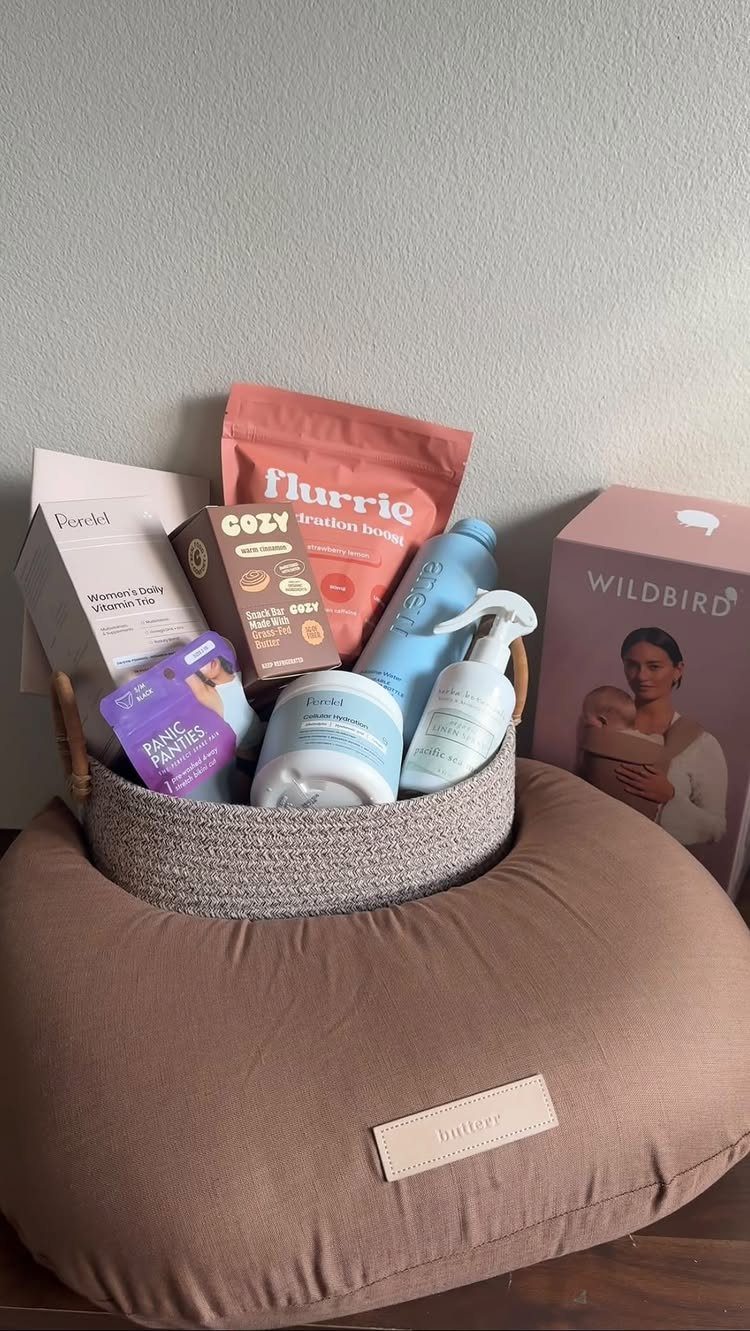 Skincare products and snacks in a grey basket resting on a nursing pillow.