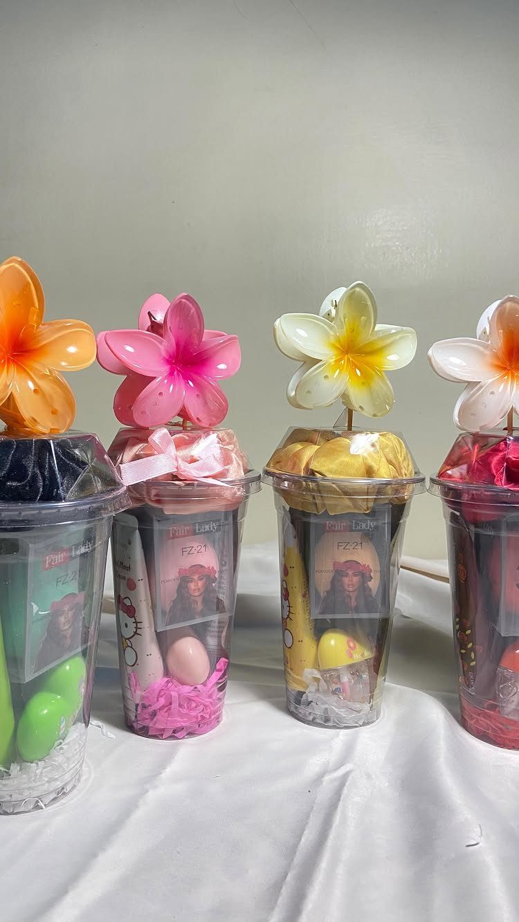 Four decorated gift cups with colorful candies and artificial plumeria flowers on top.