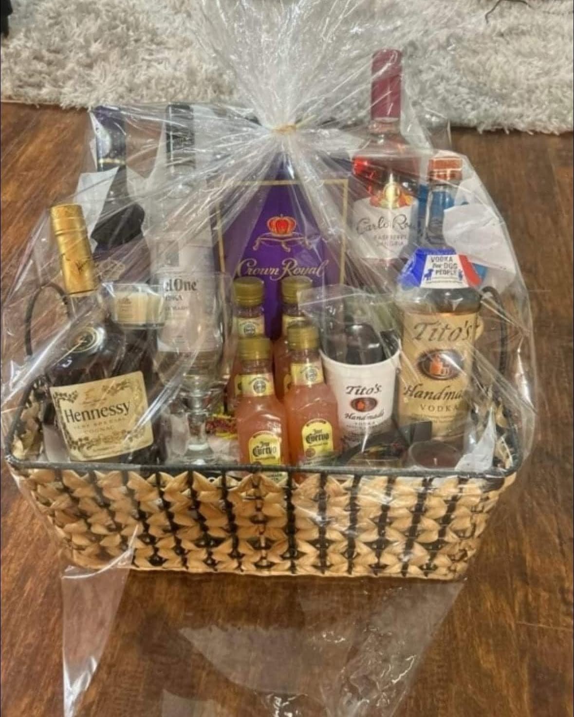Wicker gift basket filled with various liquor bottles wrapped in clear cellophane.