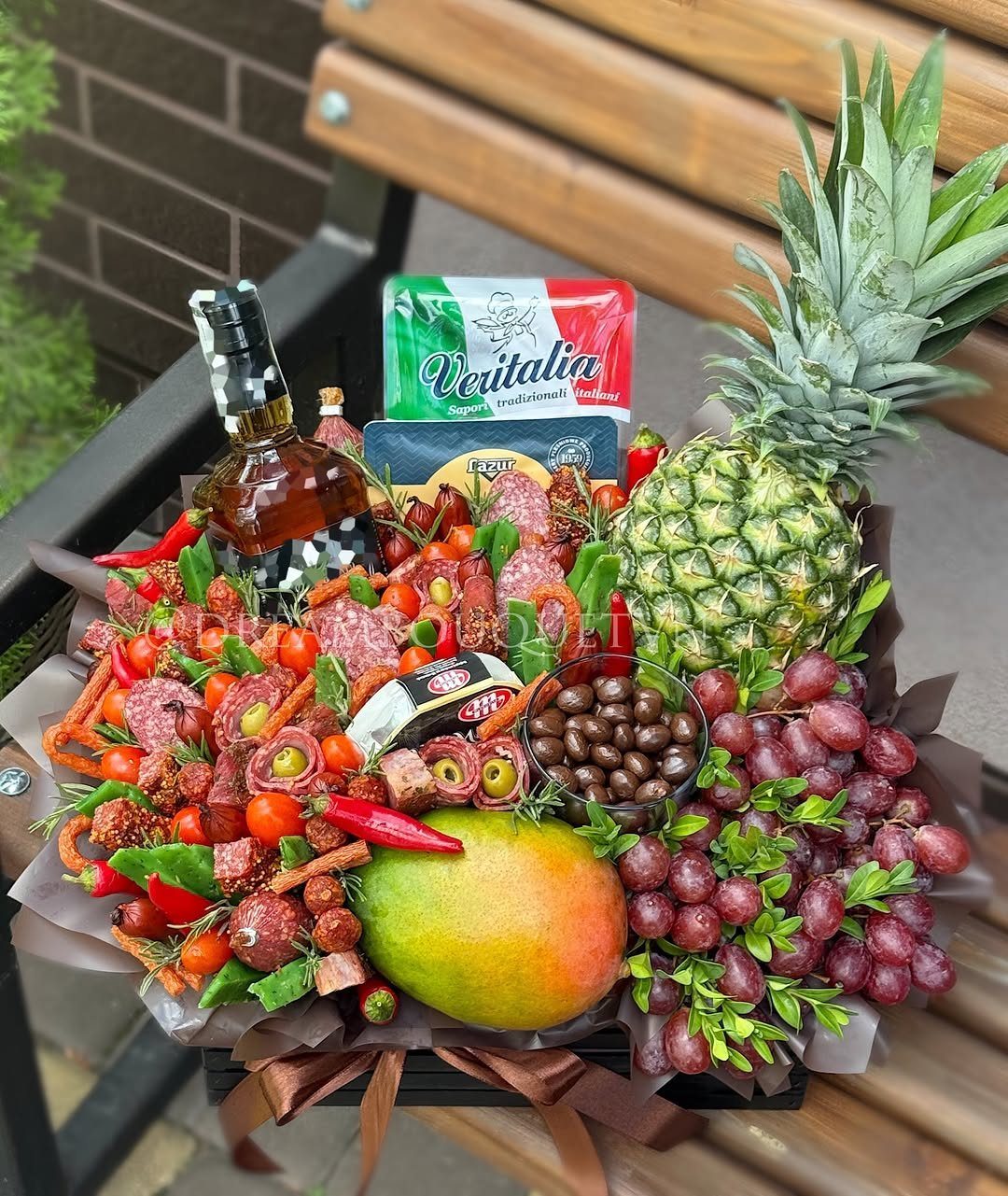 Gourmet gift basket with liquor, cured meats, cheeses, pineapple, mango, and red grapes.