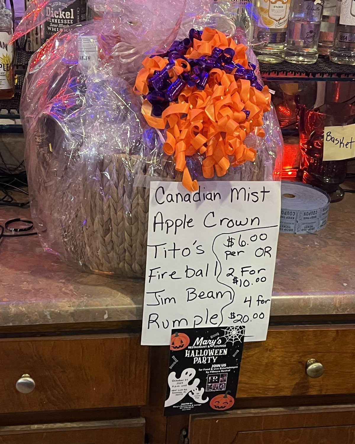 Cellophane wrapped gift basket with orange bow and a handwritten liquor price list.
