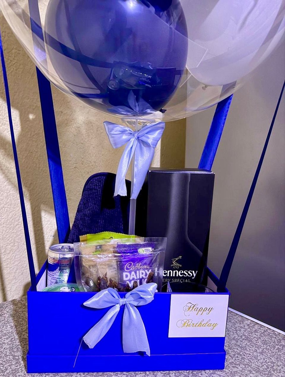Blue birthday gift box with Hennessy cognac, snacks, and a large decorative balloon.
