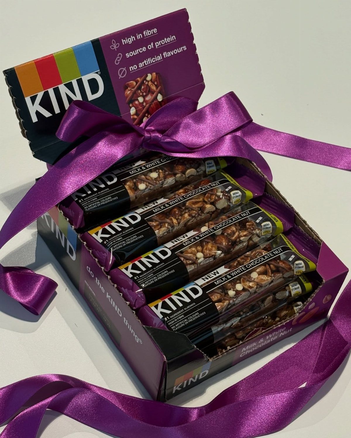 Kind bars in a box tied with a large purple satin ribbon bow.