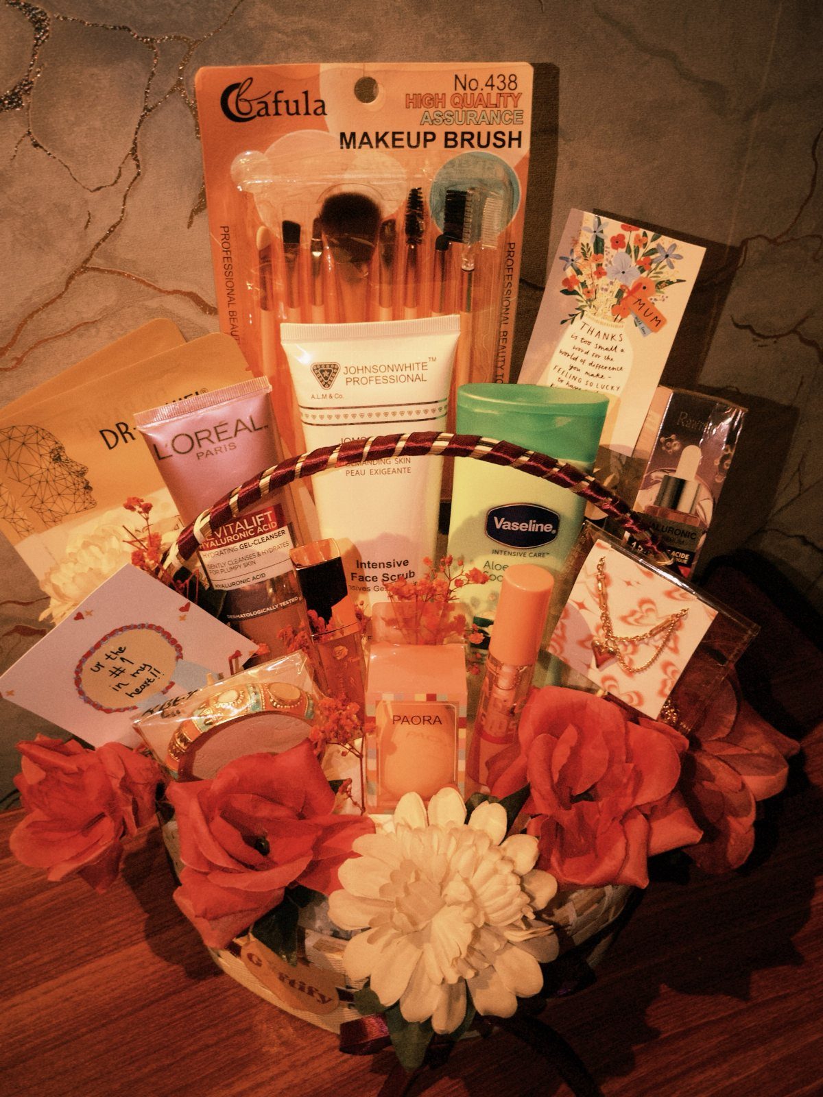 Gift basket with beauty products, makeup brushes, and red and white artificial flowers.