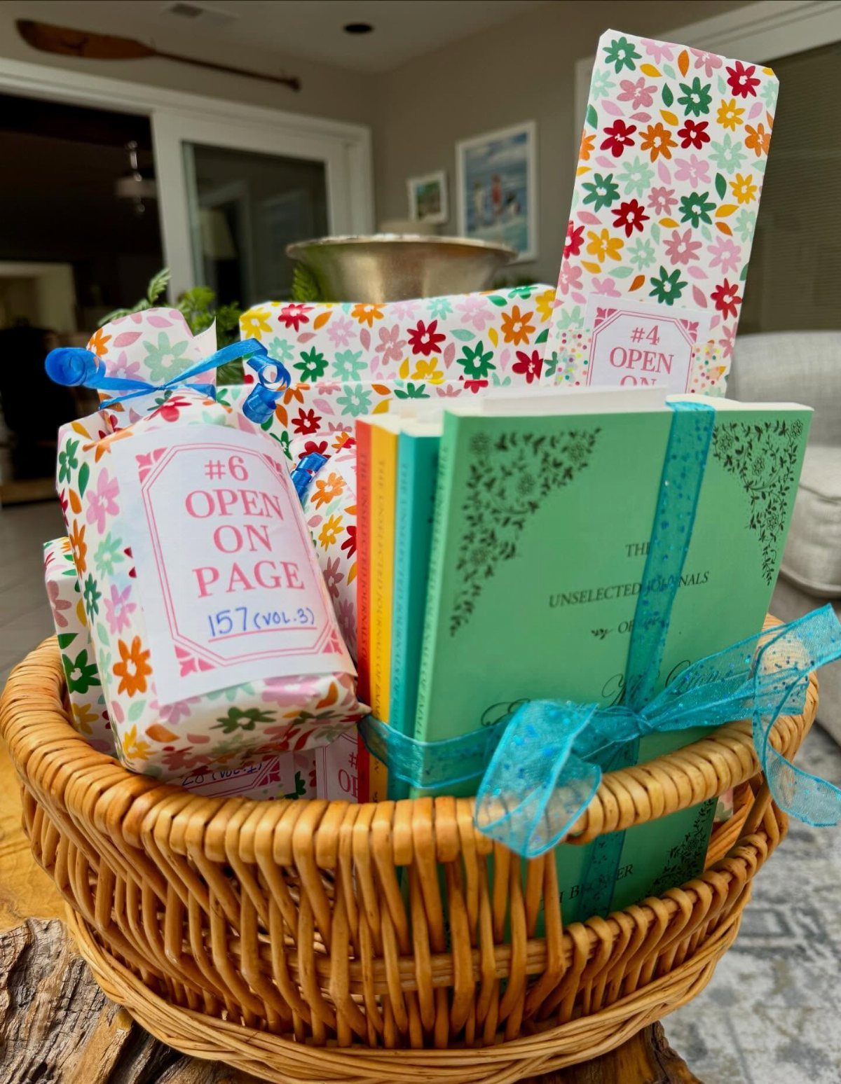 Wicker gift basket filled with floral wrapped packages and a stack of books.