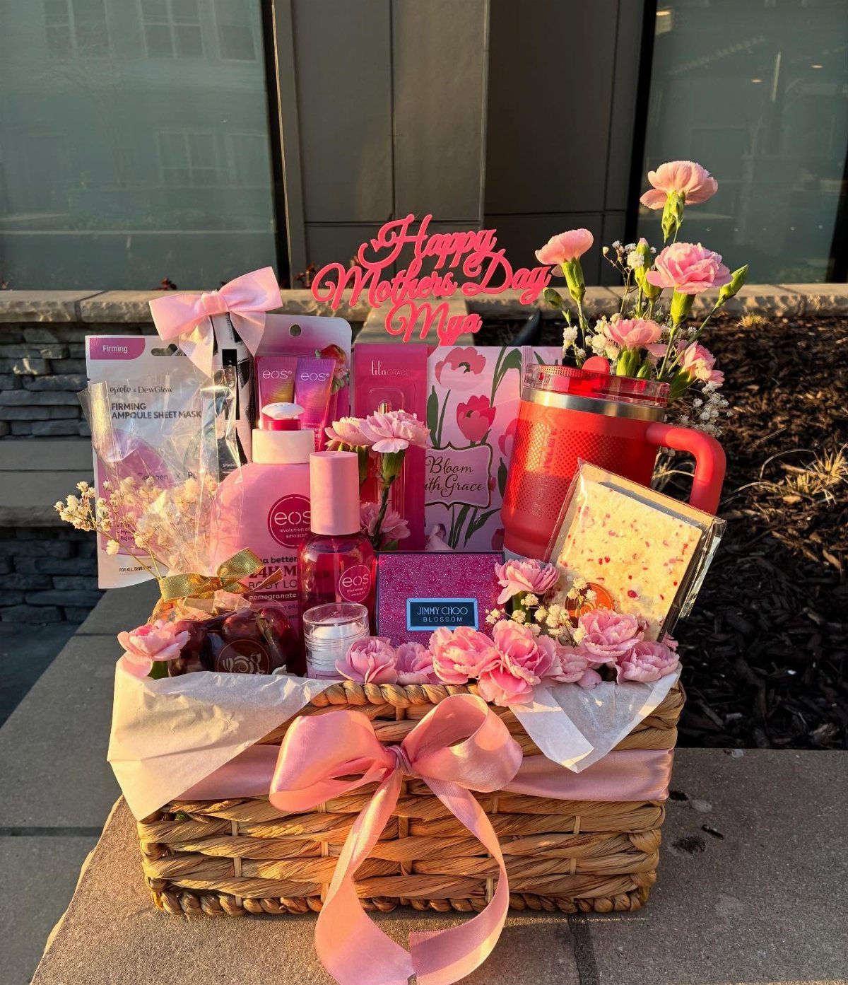 Wicker gift basket filled with pink spa products, flowers, and Mother's Day sign.