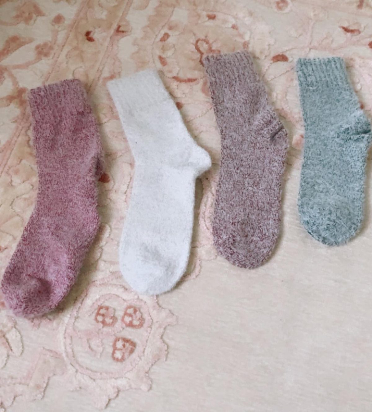 Four pairs of thick knitted socks in pastel colors on a patterned rug.