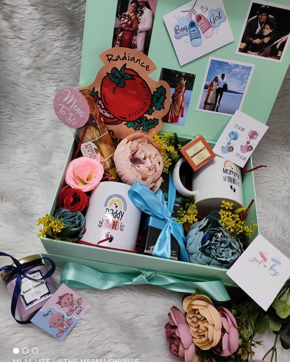 Gift box for a mother-to-be containing mugs, flowers, and personal photographs.