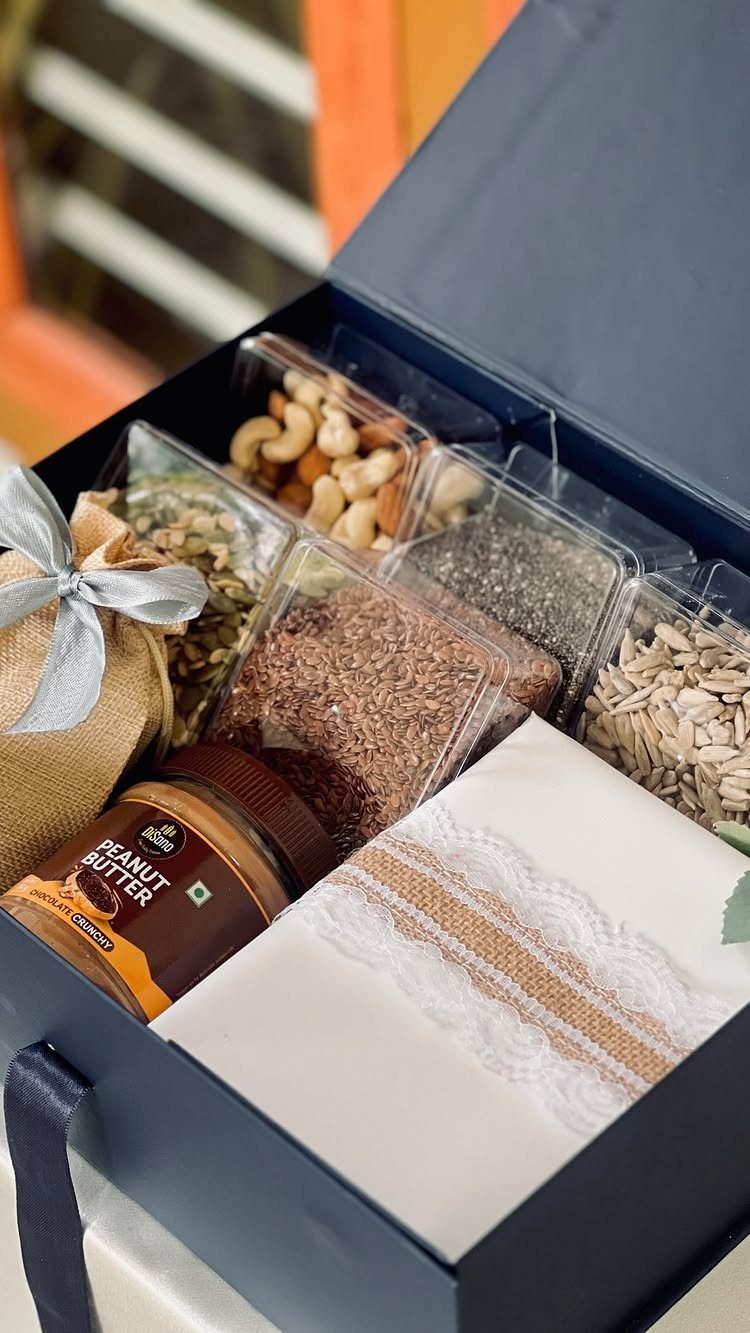 Dark blue gift box filled with nuts, seeds, peanut butter, and a lace cloth.