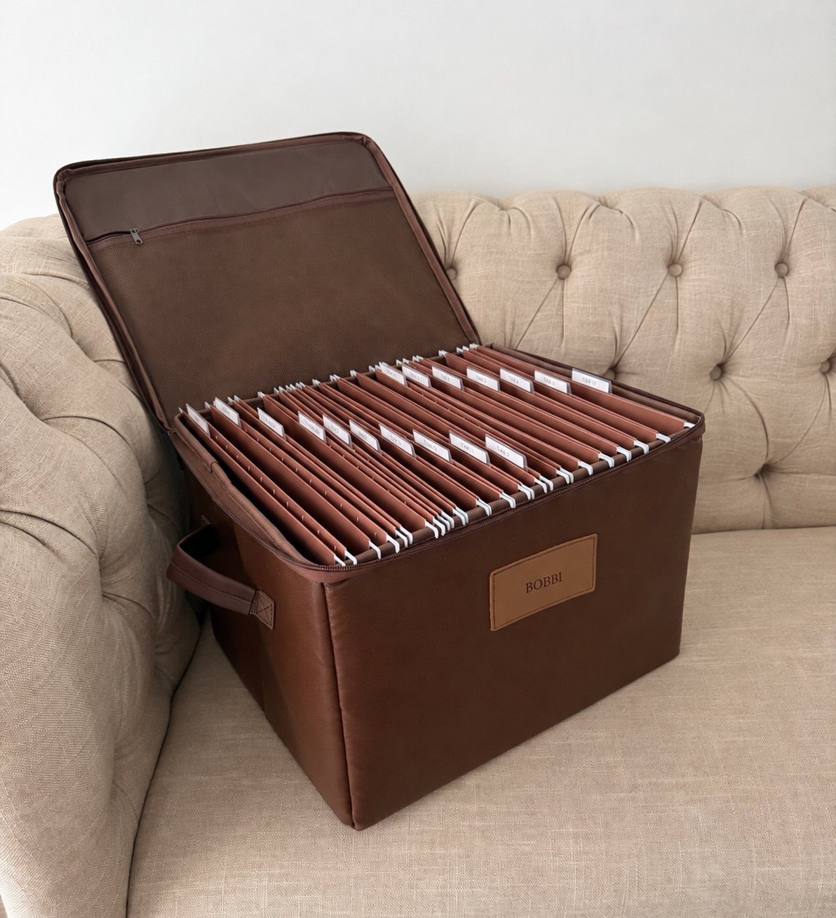Brown leather storage box with organized dividers sitting on a beige tufted sofa