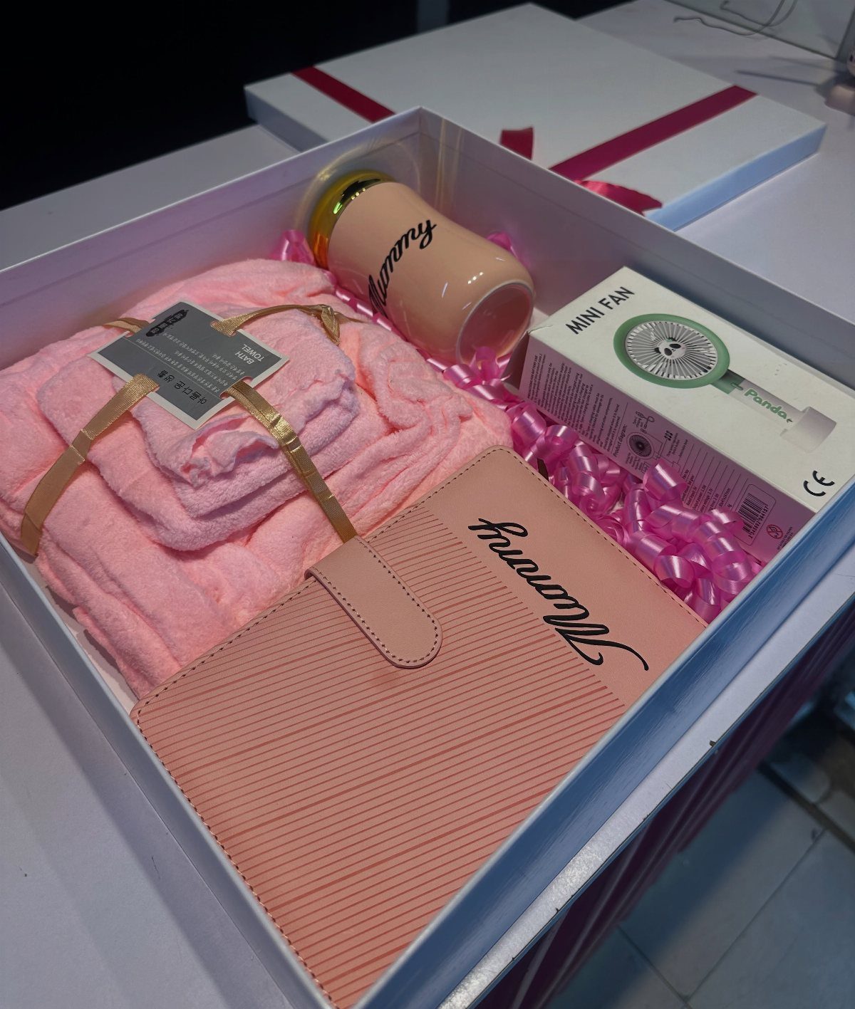 Pink themed mommy gift basket with notebook, tumbler, blanket, and mini fan.