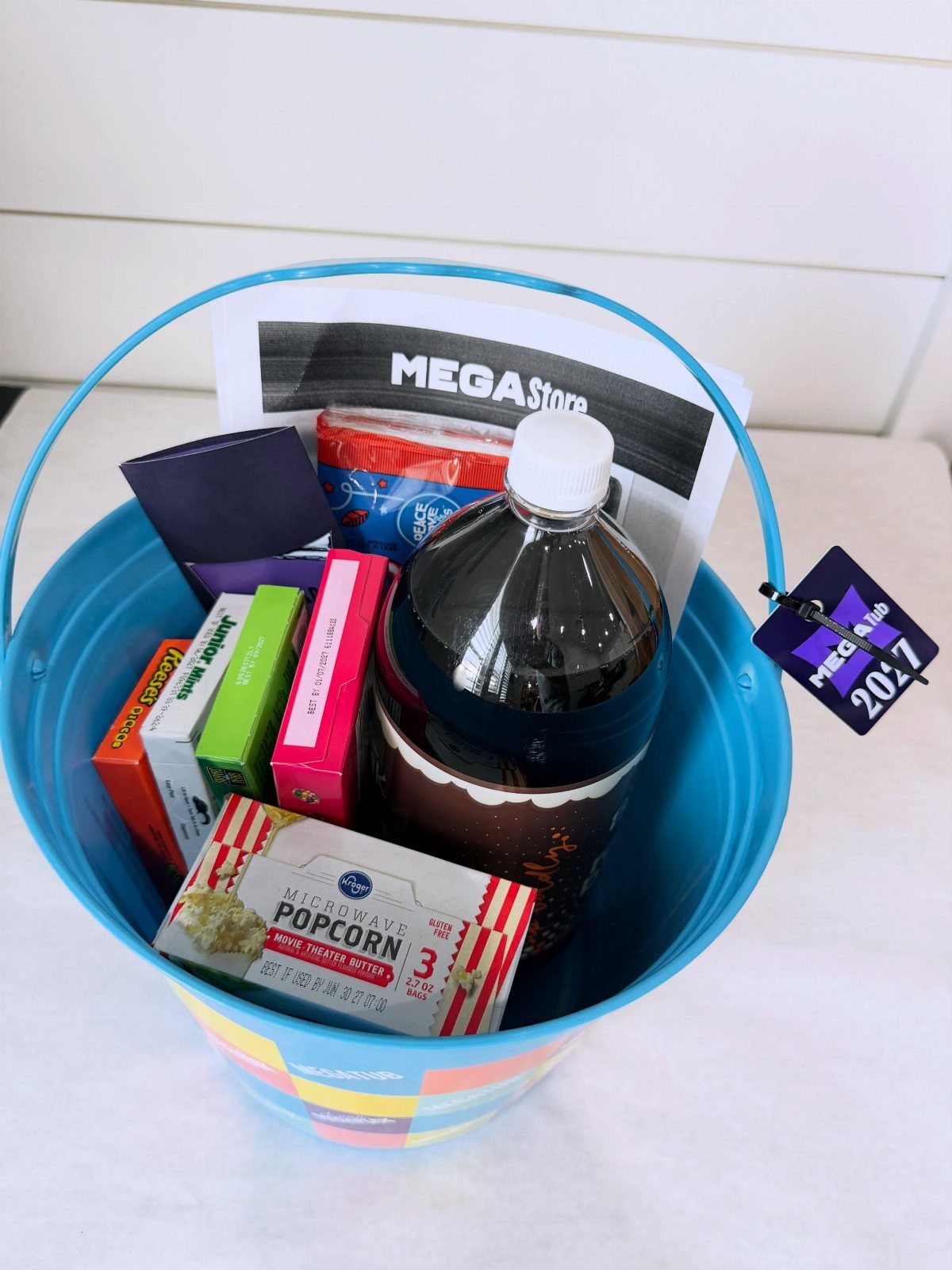 Blue bucket filled with popcorn, soda, and candy for a movie night basket.
