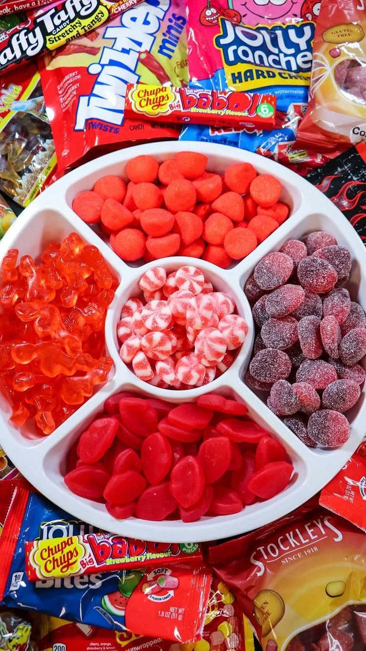 Assorted colorful gummy candies in a white divided tray surrounded by candy wrappers.