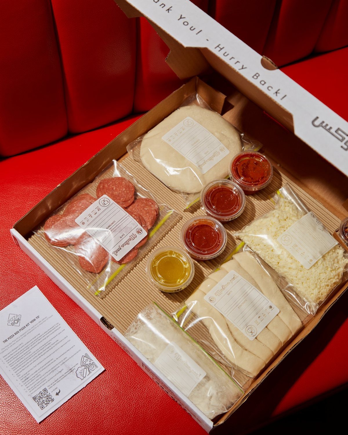 Pizza kit in a cardboard box with dough, pepperoni, cheese, and sauce.